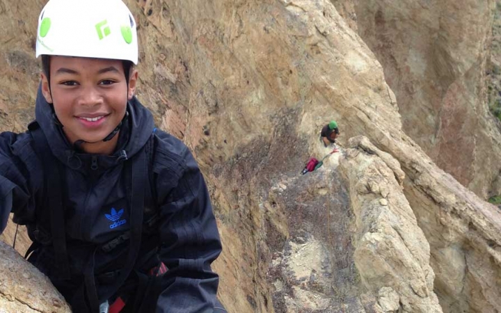 A young person wearing safety gear smiles at the camera amongst a rocky landscape.